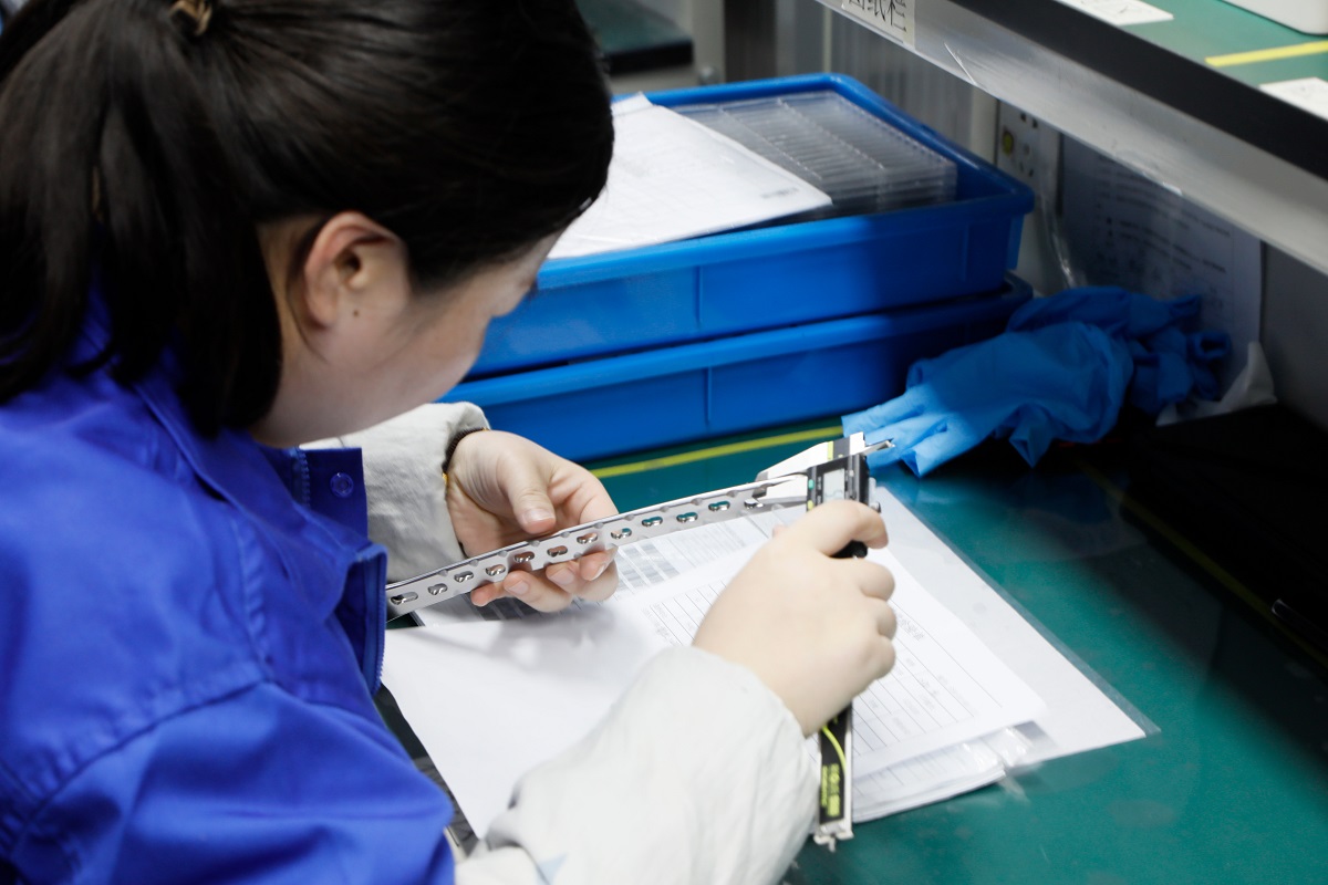Titanium trauma locking plates and screws with metrology tools on a surgical tray, suggesting OEM/ODM manufacturing precision.